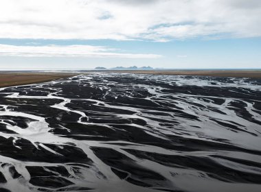 İzlanda Vestmannaeyjar 'daki buzul nehir deltasının okyanusa dökülen siyah kum desenli görüntüsü. Ham toprak, iklim güçleri, su sistemleri, doğal tasarım ve kutup minimalizmi kavramı
