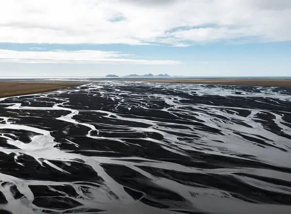İzlanda Vestmannaeyjar 'daki buzul nehir deltasının okyanusa dökülen siyah kum desenli görüntüsü. Ham toprak, iklim güçleri, su sistemleri, doğal tasarım ve kutup minimalizmi kavramı
