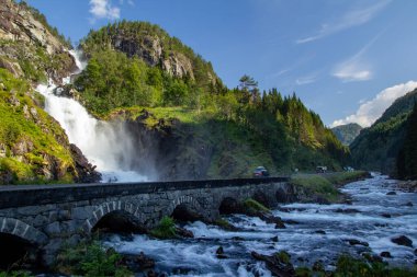 Su, yükselen bir şelale olan Latefossen 'e hücum eder. Arabalar akan bir nehir ve yemyeşil yamaçlar boyunca taş bir köprü boyunca ilerlerken güneş ışığında sprey dansı yapar..