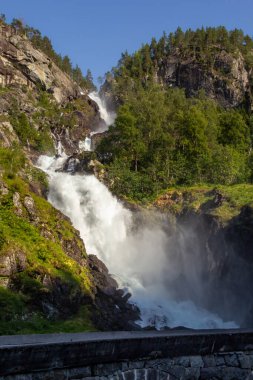Sersemletici bir şelale sarp kayalıklardan aşağı yuvarlanıyor. Etrafı canlı yeşilliklerle çevrili. Sis ve berrak mavi gökyüzünün altında sakin bir atmosfer yaratıyor..