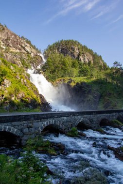 Latefossen, verimli yeşilliklerle çevrili kayalık dağlardan güçlü bir şelale düşüyor. Norveç 'te doğa ve tarihi birbirine bağlayan tuhaf bir taş köprü nehri kaplar.
