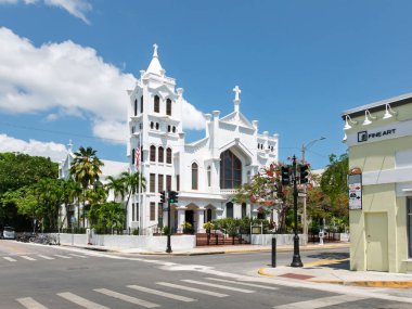 Key West, FL, ABD 13 Mayıs 2022: St Paul 's Episcopal Kilisesi yoğun bir kavşakta dikkat çekiyor. Güneş ışığı, bereketli palmiye ağaçları ve parlak çiçeklerle çerçevelenmiş beyaz mimariyi aydınlatır..