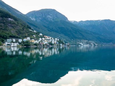 Renkli evler, Norveç 'in Odda kentindeki sakin Hardangerfjord hattında durgun sulara yansıyor ve arka planda görkemli dağlar yükseliyor.