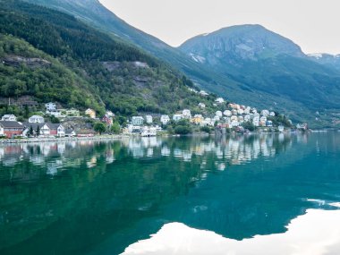 Odda 'daki güzel evler, yemyeşil dağlarla çevrili Hardangerous fijord' un hizasında. Sakin sular, canlı binaları mükemmel bir şekilde yansıtıyor. Resmedilmeye değer bir manzara oluşturuyor.