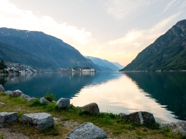 Odda 'da renkli bir günbatımının altında yükselen dağlarla çevrili sakin bir Hardangerous fjord' un nefes kesici manzarası..