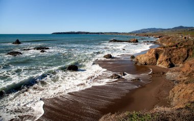 Dalgalar, Cambria, California 'da kışın engebeli bir kıyı şeridine yuvarlanarak kayalara çarptıklarında beyaz köpük oluşturur.