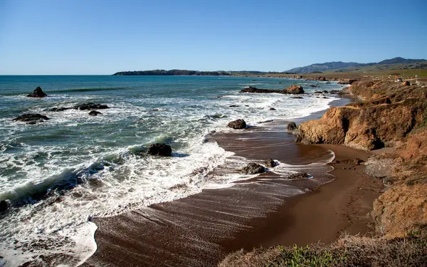Dalgalar, Cambria, California 'da kışın engebeli bir kıyı şeridine yuvarlanarak kayalara çarptıklarında beyaz köpük oluşturur.