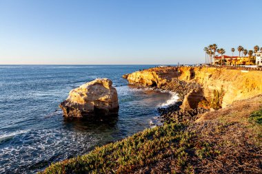 Dalgalar kayalıklara vuruyor, altın yansımaları, Sunset Cliffs, San Diego, CA 'nın yumuşak akşam ışığında parıldıyor..