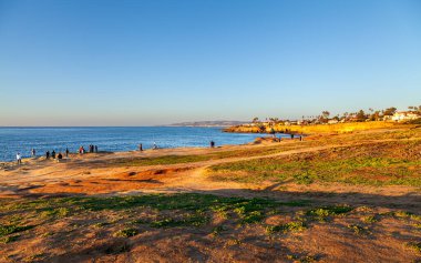 Güneşin sıcacık parıltısı Sunset Cliffs 'e sihirli bir ışık saçar. İnsanlar gün batımını izlemek için toplanır..