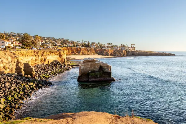 Altın saat boyunca sakin su ve yumuşak ışık kayalıkları ve kumlu sahili aydınlatıyor. Sunset Cliffs, San Diego, California 'da huzurlu manzaralar sunuyor.