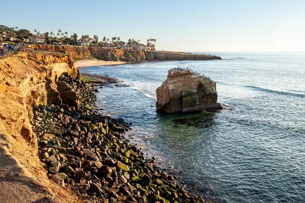 Günbatımının altın ışığı, Sunset Cliffs ve Ross Rock 'ın güzelliğini arttırır. San Diego' daki engebeli kıyı şeridini ve arka plandaki sakin sahili ön plana çıkarır.