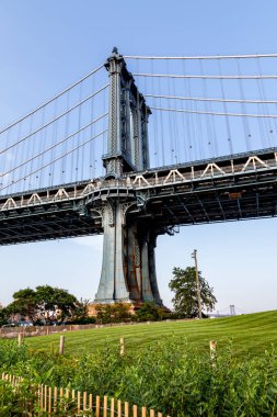 Manhattan Köprüsü 'nün demirden yapısını gösteren çarpıcı manzarası New York' ta güneşli bir günde canlı yeşillik zeminine vurgu yapıyor ve şehir güzelliğini vurguluyor..