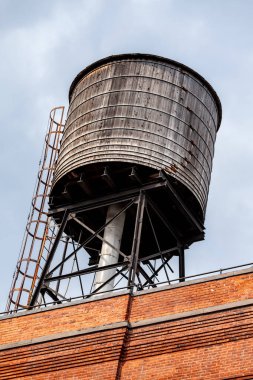 Manhattan, New York 'ta yıpranmış tuğladan bir binanın tepesinde kırsal ahşap bir su kulesi var. Yapı özellikleri ve tarihi cazibesini vurgulayan metal bir merdiven..