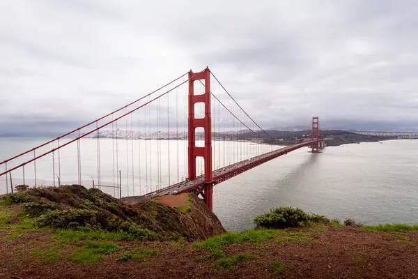 Golden Gate Köprüsü körfezin üzerinde, yemyeşil tepelerle çevrili duruyor. Yumuşak bulutlar gökyüzünde asılı, aşağıdaki sakin suyu yansıtıyor. Bu görüntü San Francisco 'nun özünü yansıtıyor..