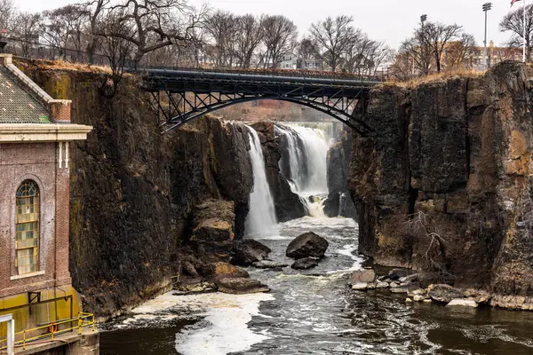 15 Mart 2025, Paterson, New Jersey, ABD: Great Falls 'un ve Passaic Nehri' ndeki eski hidroelektrik santralinin editörlük manzarası. Tarihi bölgeyi engebeli kayalar, metal köprüler ve şehir elementleri tanımlıyor.
