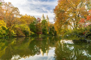 Renkli sonbahar yeşillikleri New York 'taki ağaç tepelerinin üzerinde yükselen gökdelenle Central Park gölünün manzarasını çerçeveler..