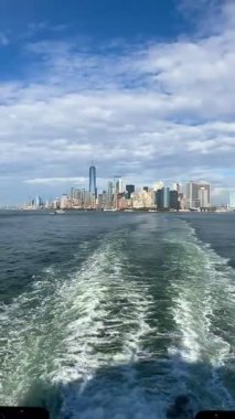 Staten Island feribotu Manhattans Finans Bölgesi 'nden kalkıyor. Beyaz bulutlu çarpıcı mavi gökyüzü ikonik New York şehrinin siluetini yükseltiyor..
