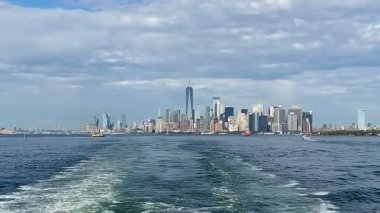 Staten Island feribotu hareket ederken Manhattan ufuk çizgisinin nefes kesici panoramik görüntüsü. Uyanış, bulutlu ve mavi gökdelenlerle çelişiyor..