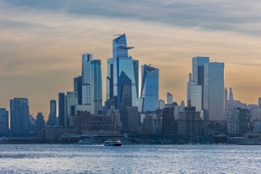 Manhattan silueti üzerinde canlı bir gün doğumu Hudson Nehri boyunca Hoboken, NJ 'den izleniyor, parlayan bulutları yakalıyor ve sabahın erken saatlerinde suya yansıyan ışığı yansıtıyor..
