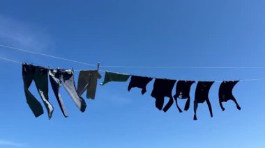 Açık mavi gökyüzünün altında yavaşça sallanan günlük kıyafetlerin basit yaşam, sürdürülebilirlik ve çevre dostu kurumayı simgeleyen 12 saniyelik videosu..