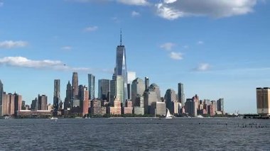 Hoboken, NJ, ABD 26 Mayıs 2025: 15 New York Citys Lower Manhattan siluetinin güneşli bir günde Hudson Nehri 'nin karşısından izlenen videosu. Dünya Ticaret Merkezi 'nin belirgin bir şekilde görülebildiği ikonik manzara, sakin su ve açık mavi gökyüzü.
