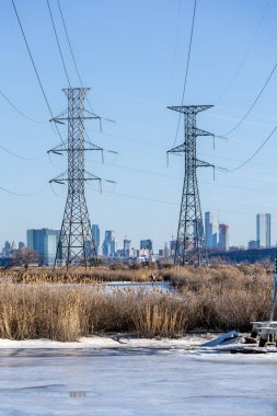 İki yüksek güç iletim kulesi, ön planda donmuş su ve bataklık ile ufuk çizgisine hakim. Manhattan ufuk çizgisi kışın soğuk gökyüzünün altında görünür..