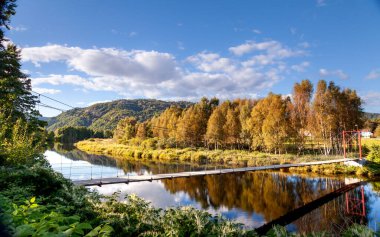 Norveç 'in güneyinde Lyngdal' ın merkezinde hareketli sonbahar ağaçlarıyla çevrili asma bir köprünün altından sakin bir nehir akar. Berrak mavi gökyüzü su yüzeyine yansıyarak doğal güzellikler açısından zengin bir kırsal alan oluşturur..