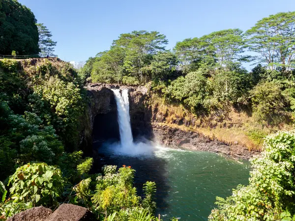 Büyük Ada, Hawaii 'deki Hilo' da gökkuşağı şelaleleri, canlı yeşil yeşillikler ve parlak mavi gökyüzü ile çerçevelenmiş, nefes kesen doğal güzelliği yakalıyor..