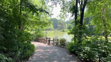 New York City, New York, ABD, 25 Temmuz 2025. Manhattan 'da yaz manzarası, Central Park gölünün sakin manzarası, uzakta kayıklar, yapraklı bir patika boyunca ağaçlar tarafından çerçevelenmiş. Yazı. 