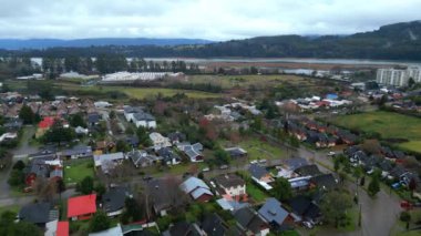İnsansız hava aracı görüntülerinde Valdivia, Şili 'deki bir banliyö mahallesinin temiz bir yerleşim yeri ve parlak renkli çatıları olan evleri görülüyor. Evlerin ötesinde bir şey var.