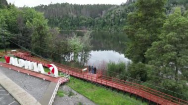 Valdivia, Şili 'deki nehir kenarı izleme güvertesinin havadan görünüşü, kırmızı şemsiyeli bir Valdivia işareti içeriyor. Güverte yemyeşil ile çevrili, sakin bir nehre bakıyor.