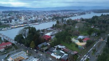 Şili Valdivia 'nın geniş panoramik görüntüsü, kameranın düzgün bir şekilde sağa döndüğü, nehir kenarının detaylı bir görüntüsünü ortaya koyuyor. Sahnede trafik dolu bir köprü var.