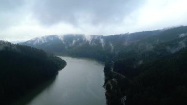 Yoğun ormanlık tepelerde dolaşan sislerle kaplı bir nehrin ruhani manzarası. Sis, ağaçlarla kaplı yamaçlara yapışarak atmosferik bir manzara yaratıyor. Sis tabakaları etrafında dönüyor.