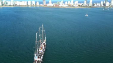 Sakin kıyı sularında huzur içinde yüzen renkli bayraklarla süslenmiş büyük bir yelkenlinin üzerinde uçan çarpıcı bir dikey hava aracı. # Dalgalı mavi deniz, güzel bir tezat oluşturuyor #
