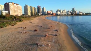 Gün batımında Punta del Este 'de sahili yakalayan güzel bir hava aracı görüntüsü. Yumuşak altın ışık kumda uzun gölgeler oluştururken, insanlar kıyı şeridi boyunca dinleniyor. Canlı bir şehir.