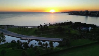 Montevideo, Uruguay 'ın Rambla' sı üzerinde çarpıcı bir günbatımı manzarası. Görüntü, Rio de la Plata 'nın sakin sularını ve kıyı bölgesinin yemyeşil sularına yerleşmiş küçük yansıtıcı bir lagünü yakalar.
