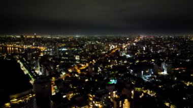 Montevideo 'nun geniş bir gece manzarası, şehrin aydınlatılmış kentsel manzarasını gözler önüne seriyor. Manzara, binaların yansımalarıyla ufuk çizgisi boyunca uzanan parlak şehir ışıklarını vurguluyor.
