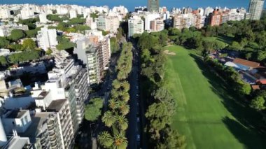 Montevideo, Uruguay 'da yüksek palmiye ağaçları olan bir bulvar manzarası. Atış, bir tarafta yemyeşil yemyeşil, bir golf sahasının el değmemiş çimleriyle çevrili canlı bir caddeyi yakalıyor.