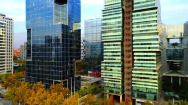 Hareketli bir finans bölgesindeki modern gökdelenlerin büyüleyici hava manzarası. Sahne, şehir manzarasını yansıtan çağdaş ofis binalarının yüksek cam cephelerini yakalıyor.
