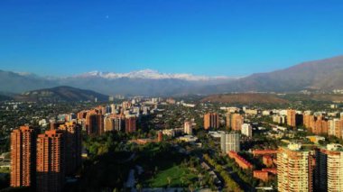 Panoramik bir hava manzarası açık bir günde çarpıcı bir sıradağ zeminiyle canlı bir şehir manzarası yakalıyor. Görüntü, yüksek binaları ve yeşil binalarıyla kentsel yerleşimi gösteriyor