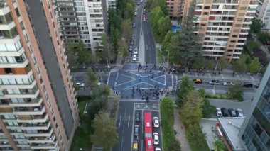 Şehir merkezindeki kalabalık bir yaya geçidini gösteren, yüksek binalarla çevrili bir hava görüntüsü. Sahne, insanlar ve araçlar arasındaki dinamik etkileşimi vurguluyor.