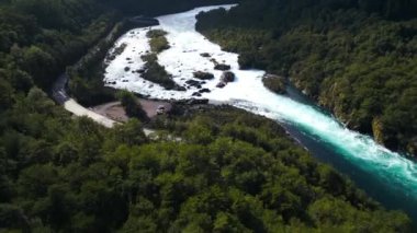 Turkuaz bir nehrin çarpıcı güzelliğini keşfedin. Güçlü akıntılarla dolu, yemyeşil bir ormanlık vadide dolanan. Bu hava görüntüsü, dinamiği vurgulayarak el değmemiş doğal manzarayı yakalar.
