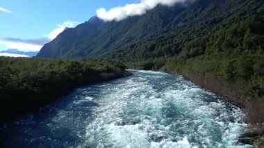 Yüksek yeşil dağlarla çevrili yemyeşil bir orman vadisinde akan hızlı akıntılarla dolu bir dağ nehrinin dramatik güzelliğinin tadını çıkar. Bu hava görüntüsü el değmemiş doğayı yakalar.