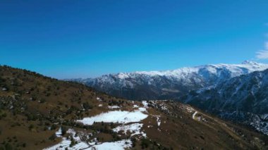 Karlı bir dağ manzarasının bu çarpıcı hava görüntüsüyle doğanın barışçıl uyumunu yakalayın. Sahne, yuvarlanan tepeler ve atların otladığı el değmemiş beyaz bir kar tarlası sergiliyor.