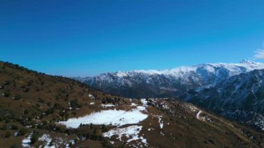 Bu sakin hava görüntüsü, otlayan atlarla benekli huzurlu bir karlı dağ çayırını yakalıyor. İnsansız hava aracı sürekli hareket ediyor, nefes kesen karlı zirveleri ve huzur dolu manzarayı gösteriyor.
