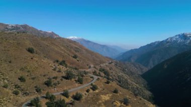Düzenli bir dron tarafından ele geçirilen güzel bir dağ vadisinin huzurlu hava manzarasının tadını çıkarın. Bu barışçıl görüntülerde engebeli arazide karlı zirveleri olan dolambaçlı bir yol görülüyor.
