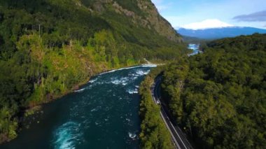 Bereketli yeşil ormanlar ve yüksek dağların arasına kurulmuş canlı bir nehrin akışını takip eden dolambaçlı bir yolun nefes kesici güzelliğini deneyimleyin. Bu hava görüntüleri uyumu yakalar.