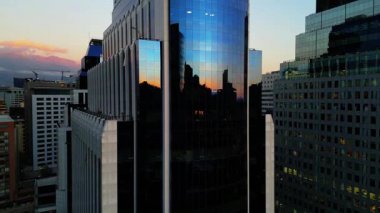 İnsansız hava aracı günbatımında Santiago Şili 'de modern bir cam ofis kulesini çekiyor. Yansıtıcı cephe, ufuk çizgisini, yakınlardaki binaları ve And Dağlarını akşam ışığında yansıtıyor.