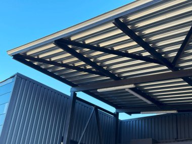 Bir şirket binasının metal kiremit çatısının yakın çekimi. Paneller pürüzsüz, desenli desenli, metalin dayanıklılığını ve hava direncini gösteriyor..