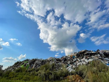 Açık güneşte paslanan plastik torbalar ve metal plaketlerle dolu bir atık deposu.